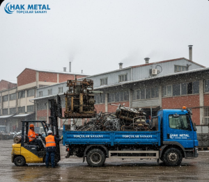 Karlı bir kış gününde Bayrampaşa Topçular Sanayi Sitesi'nde, işçiler forklift ile eski tekstil makinelerini ve hurda parçaları Hak Metal logolu mavi kamyona yüklüyor.