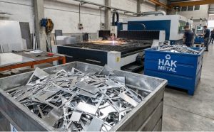 Metal işleme atölyesinde CNC lazer kesim makinesi yanında Hak Metal hurda konteynerine biriktirilmiş alüminyum imalat artıkları.